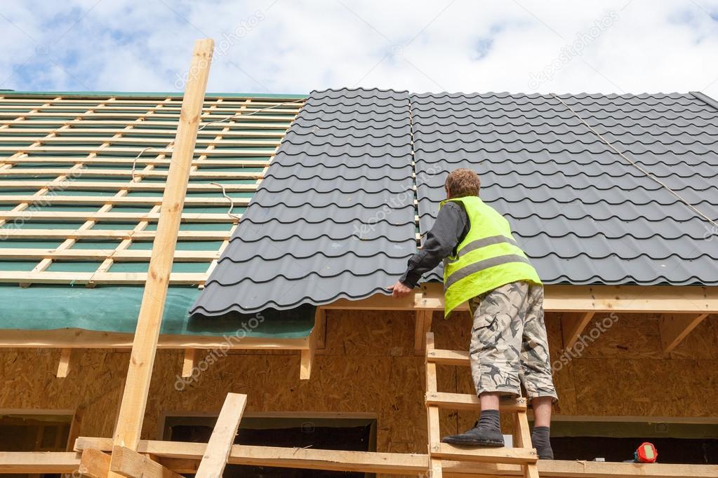 Roofer worker installing a metal tile on a new wooden house