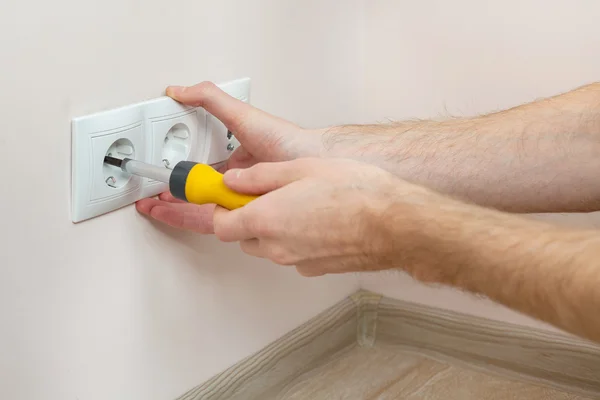 As mãos de um eletricista instalando uma tomada de energia de parede com chave de fenda — Fotografia de Stock