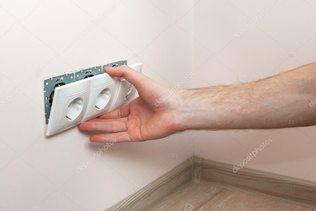 The hands of an electrician installing a wall power socket