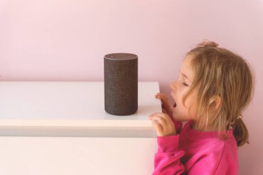 Küçük kız Amazon Alexa Echo Dot ile konuşuyor. Çocuklar için eğitim programı. Küçük kız Alexa 'yla konuşuyor ve ona emirler verip neyi açacağını söylüyor.