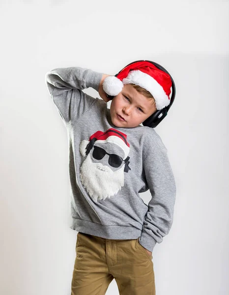 Vánoční svátky. Stylový chlapeček ve sluchátkách poslouchající hudbu ve vánočním svetru. Populární hudební a technologický koncept — Stock fotografie