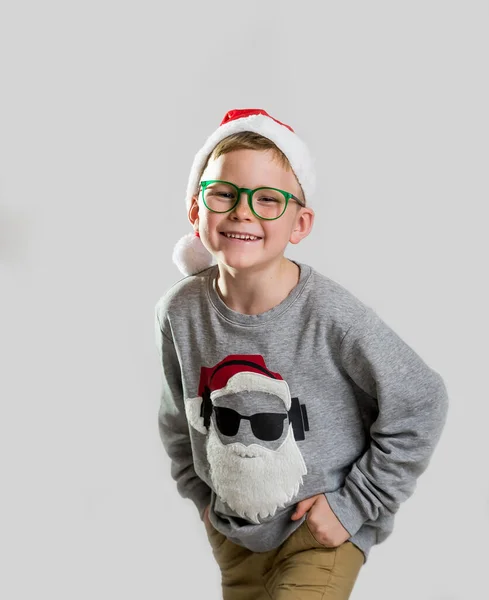 Wesołych Świąt i szczęśliwego Nowego Roku. Szczęśliwy uśmiechnięty i zaskoczony dzieciak w czerwonym świątecznym kapeluszu. Wesoły uśmiech małego chłopca otwiera usta w zaskoczeniu. Szkoła stylowy chłopiec w nowoczesnym swetrze. — Zdjęcie stockowe