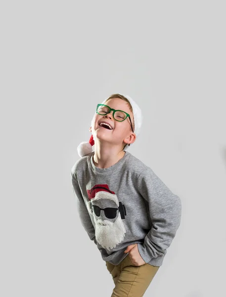 快乐的男孩穿着红色圣诞服装笑着 情绪化的孩子在等待礼物 戴着红帽子的学童和穿着毛衣的圣诞老人 圣诞快乐 新年快乐 — 图库照片