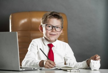 Çocuk büyüyünce nasıl zengin olabilir? Hesapla ve domuz bankasına para yatır. İşletme okulu ve gelecek için online finansal eğitim kursu. Patron koltuğunda dizüstü bilgisayarla oturuyor.