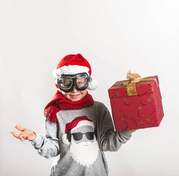带着圣诞礼物的快乐孩子孩子在家里玩的很开心戴着圣诞礼帽的时髦滑稽孩子手里拿着圣诞礼物 毛衫上有圣诞老人脸的小男孩表现出肌肉 目前的概念 — 图库照片