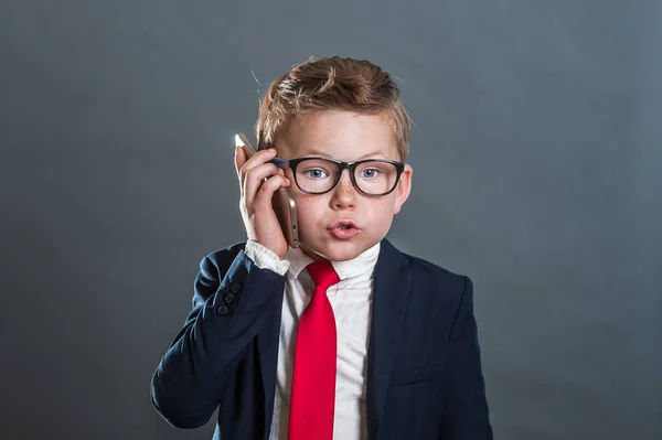 回学校去照片上的小商人 有信心的小学生穿着西服 手里拿着电话 小孩在用智能手机说话领队 — 图库照片