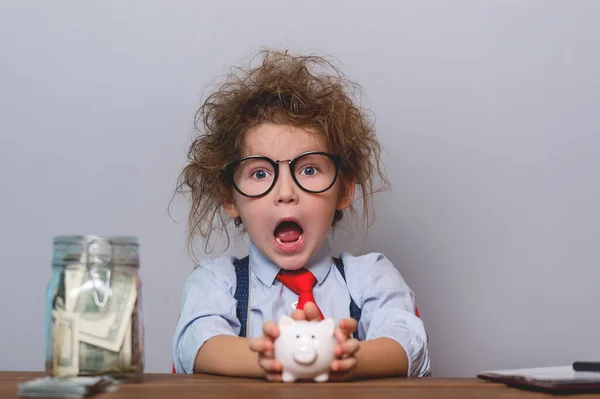 Kid and money. Funny child plays with money. Education for little businessman how to be rich when grow up. Student in glasses and tie with piggy bank and jar full of money isolated over white