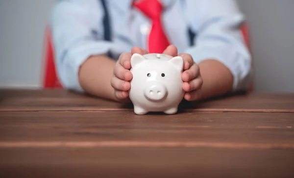 Spende aus der Wirtschaft. Sparschwein in den Händen eines kleinen Geschäftsmannes. Hand legt Münze in Biggybank Spende mit Geldstapel, Konzept Business-Finanzierung und Investition — Stockfoto