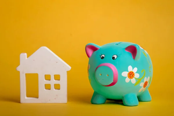Piggy bank with wooden house icon figure isolated on yellow background. Saving coin for future house. Energy efficiency green house
