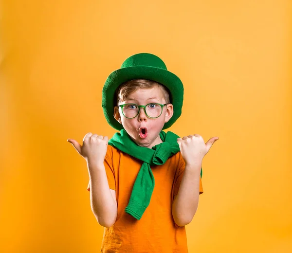 St Patricks Day. Portrait of stylish little child boy in green hat, glasses, sweater isolated on yellow. Green leprechaun. Surprised kid face pointing fingers up. Sale. Discount. March. — Stock Photo, Image