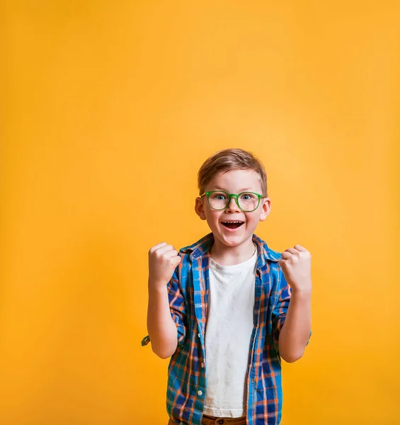 Geluksvogel met bril geïsoleerd op gele achtergrond. Zeer gelukkig en opgewonden jongen doen winnaar gebaar met opgeheven armen, glimlachen en schreeuwen om succes. Feest. Jongen superheld. — Stockfoto