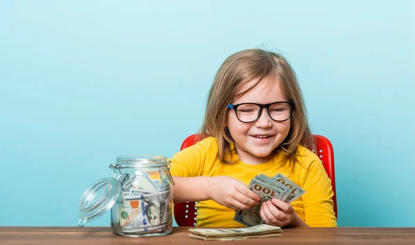 Piccolo bambino felice sorridente che tiene il vaso di beneficenza con i soldi Ragazzo con gli occhiali in camicia gialla che conta i soldi sul tavolo. Donare per beneficenza — Foto Stock