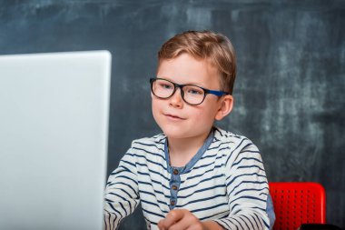 Dizüstü bilgisayar kullanan gözlüklü inek bir çocuk. Çocuğun online dersi var. Okula geri dön.