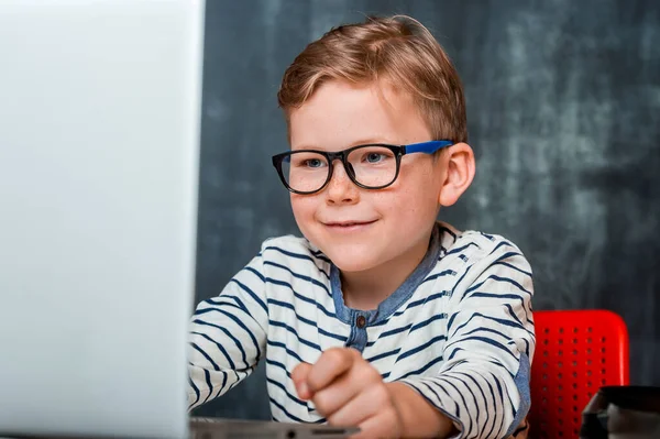 Online school education and future technology concept. little student boy with keyboard and laptop computer screen at school. Smart kid boy in eyeglasses.