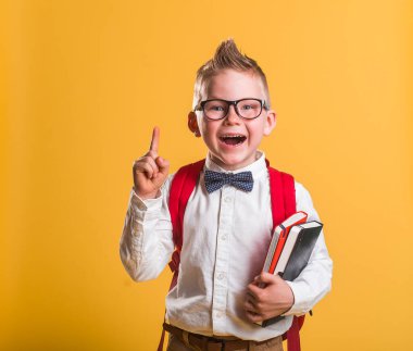 Reklam ve eğitim konsepti. Elinde not defteri ve klasörler olan gülümseyen küçük öğrenci çocuk bir şeyi işaret ediyor. Fikir yeniliği. Sarı gözlüklü çocuk. Okula geri dön.