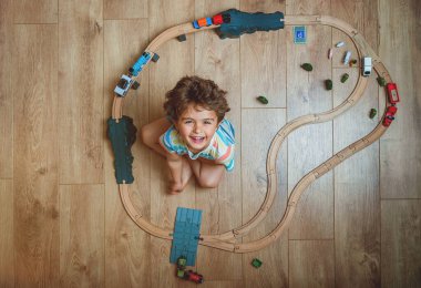 Ahşap tren setinde oynayan küçük çocuğun en iyi görüntüsü. Çocuk oyuncaklarla yerde oturuyor. Küçük çocuk için oyuncaklar. Anaokulu demiryolu inşaatı ve evdeki bloklar, kreş. Anaokulu eğitim oyunları.