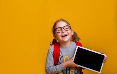 Okula dönelim. Çevrimiçi eğitim kavramı. Tablet bilgisayarlı mutlu çocuk. Çocuk ekranı gösteriyor. Sarı gözlüklü, gülümseyen kız..