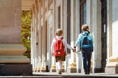 Oğlan ve kız el ele vererek okula giderler. Keyfin yerinde. Çocuk çantalı gözbebekleri. Kız gülüyor. Okula dönelim. Küçük birinci sınıf öğrencisi.