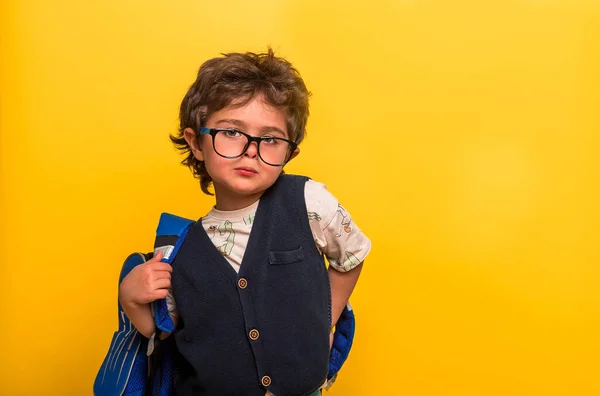 Zpátky do školy. Vtipný chlapeček v brýlích s batohem izolovaným na žluté. Dítě ze základní školy s knihou a taškou. Dítě se vrací do školy, do školky. Úspěch, motivace, vítěz, génius. — Stock fotografie