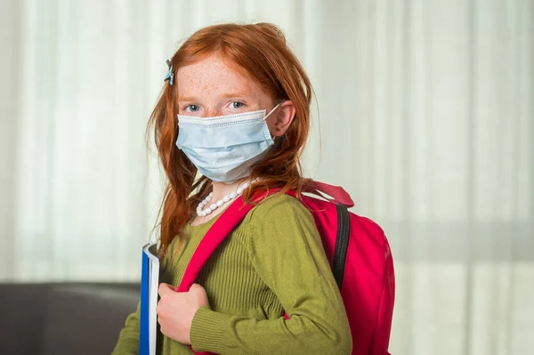Little red hair kid girl in medical mask ready for new education year. Coronavirus prevention during corona virus and flu outbreak. llness protection for child. Pupil breathes through mask in class