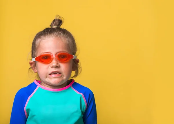 Funny little child girl in swimsuit, swimming goggles and swim cap isolated on yellow background. Funny portrait of small kid ready to swim or dive in swimming school or water park. Emotional diver. — Stock Photo, Image