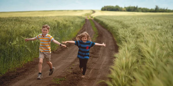 Dos niños corren en el campo de trigo. Feliz chico y chica siéntete libre y sueña con el futuro. Vacaciones de verano. Niño y niña en el camino del campo. — Foto de Stock
