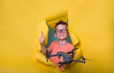 Küçük çocuk İHA 'yı tutuyor ve sarı kağıt duvarı yıkıyor. Quadcopter, helikopter, insansız hava aracı ya da uçak için uzaktan kumandalı bir çocuk. Akıllı okul çocuğu parmak kaldırıyor. Gözlüklü inek çocuk.
