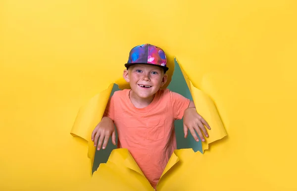 Funny stylish kid boy with missing front tooth breaks through yellow paper wall. Stylish school pupil growing. Dentist helps kids smile. Happy school child holding missing tooth. Back to school — Stock Photo, Image
