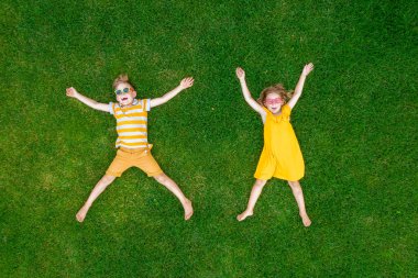 Sarı elbiseli komik çocuklar yeşil çimlerin üzerinde yatıp bağırıyorlar. Uzun ve mutlu çocuklar. Oğlan ve kız bir yıldız işareti yapar. Yaz kampı ya da tatil. İletişim konsepti