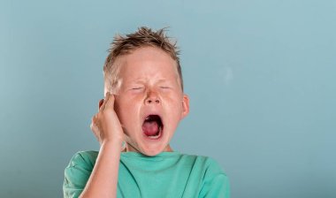 Sarışın okul çocuğu eli kulağında acı içinde bağırıyor. Çocuklarda şiddet kavramı. Çocuk bağırması. Çocuk yaralı. Kulak ağrısı