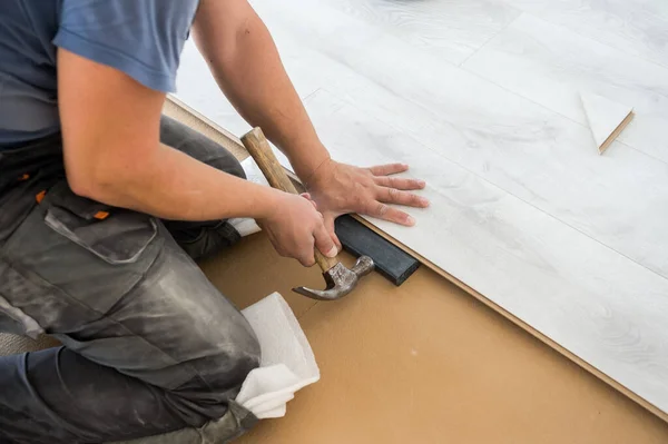 Hombre instalación de nuevo laminado en el suelo. Suelo de madera blanca. Carpintero poniendo nuevos tablones de madera en una casa nueva — Foto de Stock