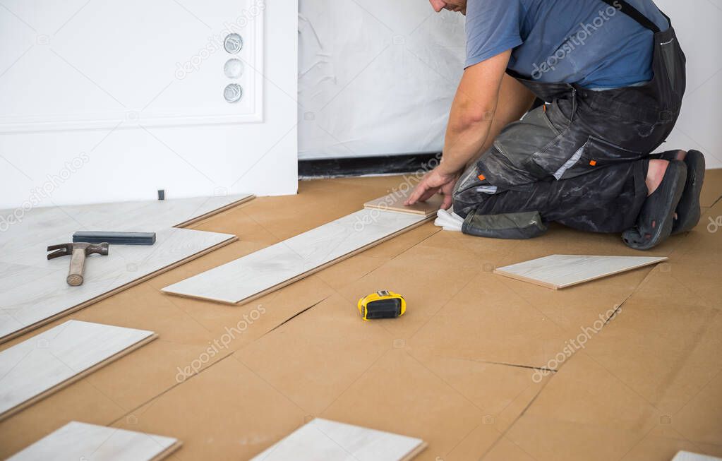 Craftsman installs light wood laminate tiles in the living area using. Young male repairman is markup a wooden panel with a pencil and a ruler before cutting. Laminate flooring, DIY