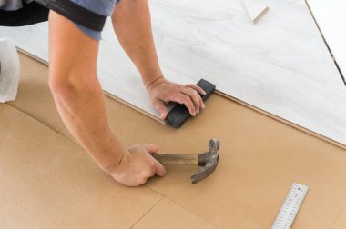 Yeni ev içinde beyaz lamine döşeme kuruluyor. Aletleri olan bir adam..