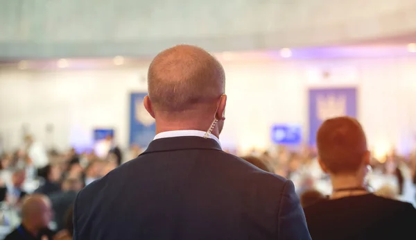 Security guard standingon public meeting. Mature security guard listening to earpiece against crowd. Secret service agent listening to his earpiece, side. secret service agent — Stock Photo, Image