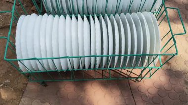 Birkaç beyaz, deniz taraklı plaka ile dolu bir sepet. Düzgün bir şekilde sıralanmış. Bu büyük bir etkinlik ya da yemek servisi için mükemmel bir düzenleme. Sepet dışarıya, dokulu, kırmızımsı kahverengi bir zemine konur..