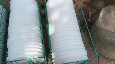 Birkaç beyaz, deniz taraklı plaka ile dolu bir sepet. Düzgün bir şekilde sıralanmış. Bu büyük bir etkinlik ya da yemek servisi için mükemmel bir düzenleme. Sepet dışarıya, dokulu, kırmızımsı kahverengi bir zemine konur..