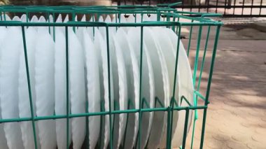 Birkaç beyaz, deniz taraklı plaka ile dolu bir sepet. Düzgün bir şekilde sıralanmış. Bu büyük bir etkinlik ya da yemek servisi için mükemmel bir düzenleme. Sepet dışarıya, dokulu, kırmızımsı kahverengi bir zemine konur..