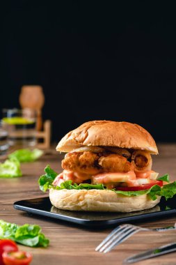 Marul, domates, soğan halkası ve mayonezli çıtır balık burger. Tahta arka planda hamburgerli balık köftesi..