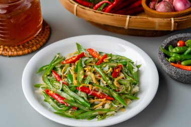 Tumis buncis ikan teri ya da tuzlanmış balık ançüezli kızarmış fasulye. Beyaz tabakta servis edilir ve gri arkaplanda izole edilir.