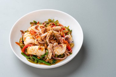 Tumis Cumi tauco ya da Baharatlı Kızarmış Mürekkep balığı beyaz tabakta servis edilir ve gri arka planda izole edilir. Tauco, mayalanmış sarı soya fasulyesinden yapılan bir macundur..