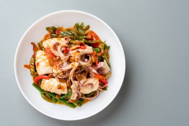 Tumis Cumi tauco ya da Baharatlı Kızarmış Mürekkep balığı beyaz tabakta servis edilir ve gri arka planda izole edilir. Tauco, mayalanmış sarı soya fasulyesinden yapılan bir macundur..