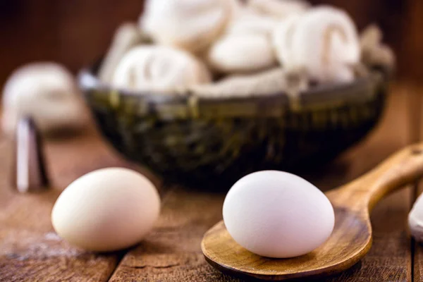 country eggs in wooden spoon, rustic kitchen setting, cookies made with eggs in the background