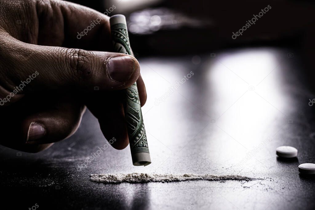 hand holding money straw to inhale a portion of cocaine, white powder to be inhaled, concept of addiction and drug addiction, dealer and sale of drugs