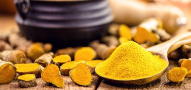 Taşralı ahşap kaşıkta zerdeçal tozu, etrafında da zerdeçal kökleri var.