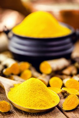 Bir kaşık zerdeçal tozu, ahşap bir kasede zerdeçal kökü.