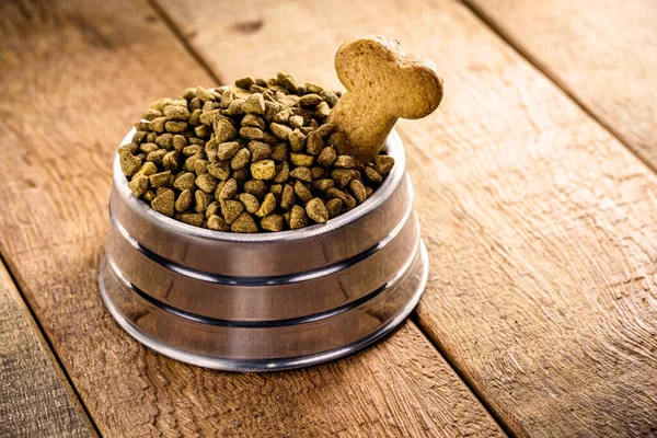 dog food with bone shaped dog biscuit in metallic bowl on wooden background, copy space