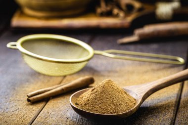 Pudralanmış ve soyulmamış tarçın kaşık ve elek, masaya serpiştirilmiş, sağlıklı pişirme konsepti.