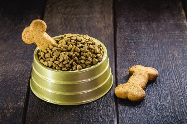 dog food with bone shaped cookie in gold bowl on wooden background, copy space