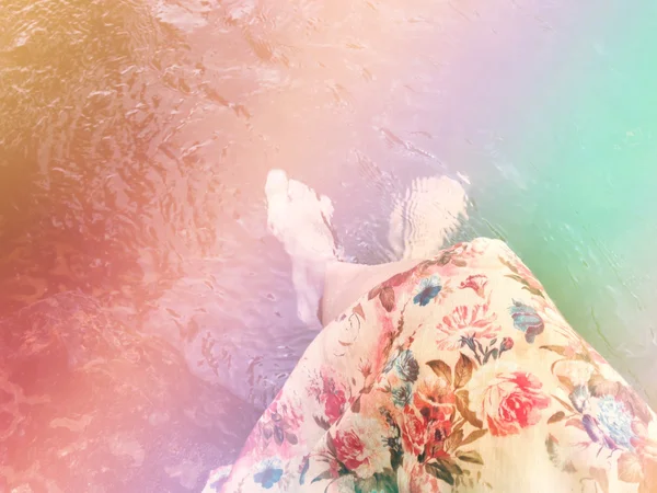 Çiçekler elbiseli kadın oturup ve suda ayak daldırma