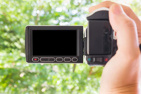 Mão tomando câmera de vídeo em branco tela preta com bokeh verde — Fotografia de Stock